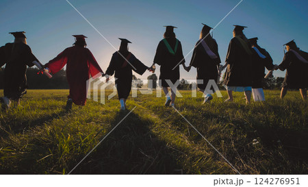 Group of graduates strolling through a field at sunset, hand in hand, celebrating their achievement 124276951