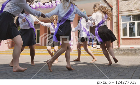 Female graduates wearing sashes and holding hands, dancing barefoot in the schoolyard, celebrating their last school day Female graduates wearing sashes and holding hands, dancing barefoot in the schoolyard, celebrating their last school day 124277015