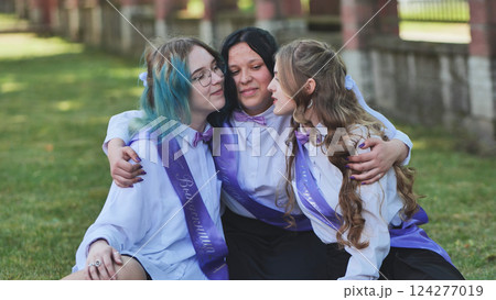 Three happy graduates hugging and celebrating their last school day, wearing purple sashes and bow ties 124277019