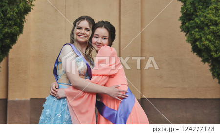 Female graduates hugging, smiling in formal attire, celebrating academic success and close bond 124277128