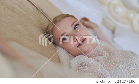 Beautiful young bride lying on bed in wedding dress, relaxing and preparing for wedding ceremony, bridal preparations, moment of peace before celebration 124277190