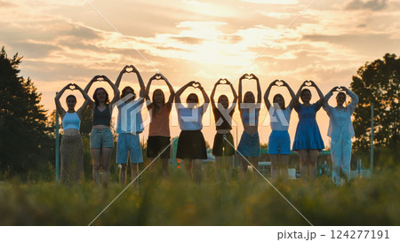 School friends forming a heart with their hands in front of a beautiful sunset, symbolizing friendship and unity 124277191