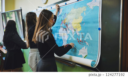 High school girls hanging a large world map on the blackboard, preparing for geography class, promoting education and teamwork 124277192
