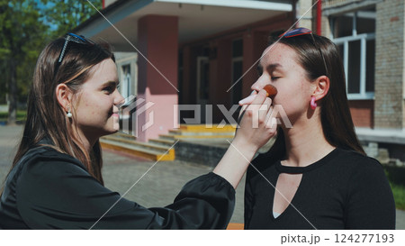 Two high school girls using a makeup brush during a school break, having fun together 124277193