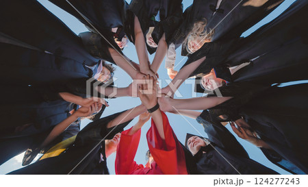 Graduates in academic gowns holding hands in circle, commemorating their academic success and the start of a new journey Graduates in academic gowns holding hands in circle, commemorating their academic success and the start of a new journey 124277243