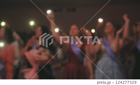 Group of students waving illuminated cell phones at graduation party, celebrating friendship and academic achievement 124277329