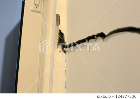 Close-up of a large crack running vertically and horizontally across an interior wall. 124277336
