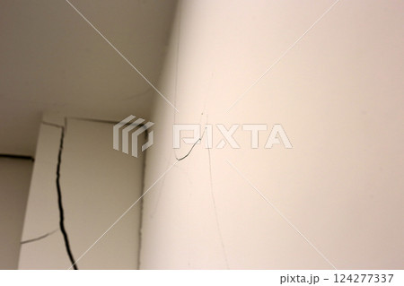 Close-up of a large crack running vertically and horizontally across an interior wall. 124277337