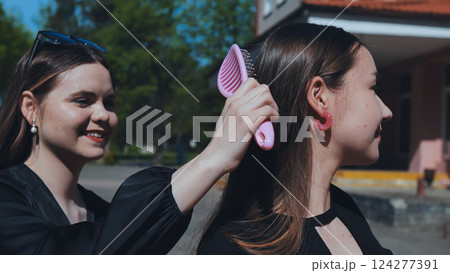 Two female students getting ready before or after school, brushing hair with pink comb, friendship and care Two female students getting ready before or after school, brushing hair with pink comb, friendship and care 124277391