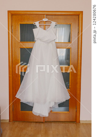 A beautiful white wedding dress hangs on a wooden 124280676