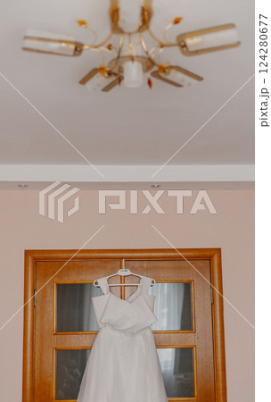 A beautiful white wedding dress hangs on a wooden 124280677