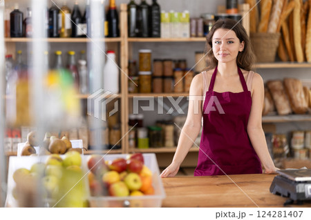 Portrait of young girl seller in an apron behind the counter of grocery store Portrait of young girl seller in an apron behind the counter of grocery store 124281407