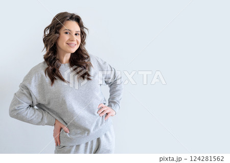 Beautiful European woman in gray knitted suit smiles and keeps hands on hips. White background. 124281562