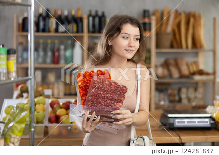 Girl pondering over choice of cured sausages in grocery shop Girl pondering over choice of cured sausages in grocery shop 124281837