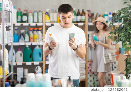 Guy view trademark sign on label, pick eco friendly sunblock cream, woman shopping in background Guy view trademark sign on label, pick eco friendly sunblock cream, woman shopping in background 124282041