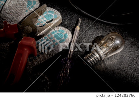 A burnt-out light bulb, a screwdriver, pliers and cloth gloves A burnt-out light bulb, a screwdriver, pliers and cloth gloves 124282766