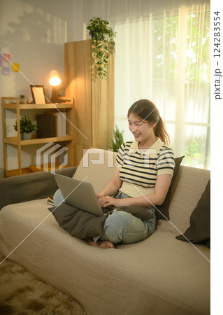 Pretty young woman browsing or working on a laptop sitting on a couch at home 124283554
