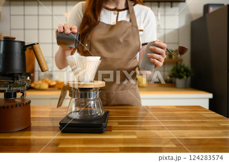 Close up of woman pours ground coffee into a dripper over glass carafe Close up of woman pours ground coffee into a dripper over glass carafe 124283574