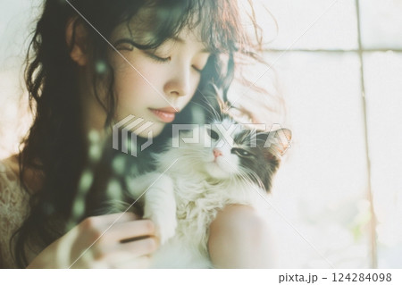 自然な美しさを持つ日本女性が窓の光の中で猫を優しく抱いている様子 124284098