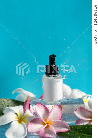 Delicate drops of water splash around a moisturizing serum alongside elegant plumeria blooms. 124286116