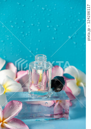 A clear serum bottle and plumeria flowers create a calming spa ambiance. 124286117