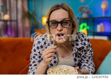 Excited amazed woman sitting on couch eating popcorn and watching interesting TV serial film game 124287450