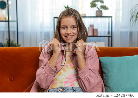 Happy girl child shouting celebrating win goal good news lottery luck victory watching TV at home Happy girl child shouting celebrating win goal good news lottery luck victory watching TV at home 124287460