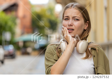 Portrait of young Caucasian woman traveler standing outdoors feeling toothache on city street Portrait of young Caucasian woman traveler standing outdoors feeling toothache on city street 124287532
