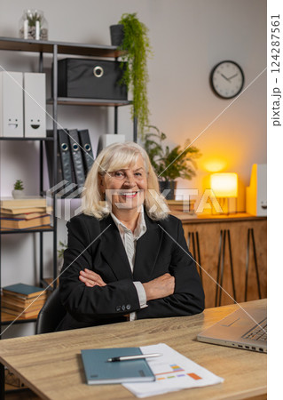 Smiling senior businesswoman using laptop computer and looking at camera at home office table 124287561