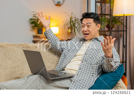 Excited man sitting on sofa using laptop receives good news victory celebrate lottery win at home 124288821