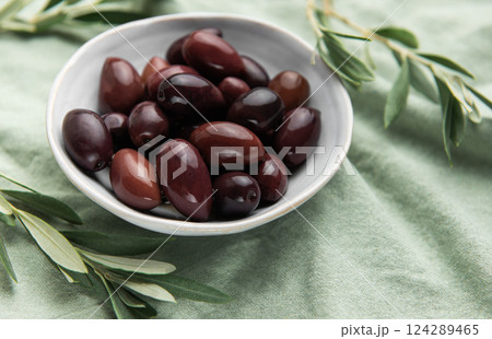 Kalamata olives with olive branches resting in a bowl on green tablecloth Kalamata olives with olive branches resting in a bowl on green tablecloth 124289465