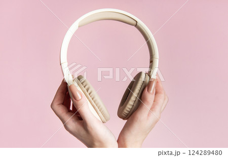 Woman holding wireless headphones on pink background 124289480
