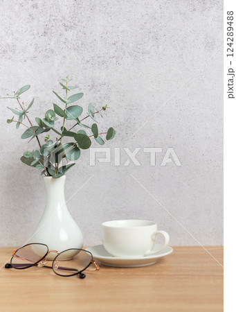 Eucalyptus branches, coffee cup and eyeglasses resting on wooden desk 124289488