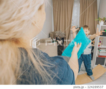 boy developing motor skills and coordination by playing on a wooden wobble board during a therapy session, interacting with a therapist 124289537