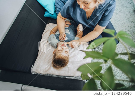 smiling boy lying on blanket during a therapy session with a female specialist in a cozy room, concept of relaxation, childhood therapy, and healthcare smiling boy lying on blanket during a therapy session with a female specialist in a cozy room, concept of relaxation, childhood therapy, and healthcare 124289540