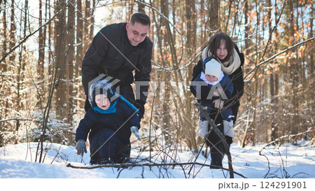 Family enjoying winter landscape, walking together through snow covered forest, sharing warmth and happiness on sunlit day 124291901