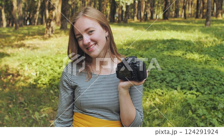 Young female photographer smiling while showcasing her camera's display in a vibrant park filled with lush green trees and grass Young female photographer smiling while showcasing her camera's display in a vibrant park filled with lush green trees and grass 124291924