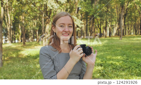 Smiling photographer gripping camera amid lush green park under bright summer sunlight Smiling photographer gripping camera amid lush green park under bright summer sunlight 124291926