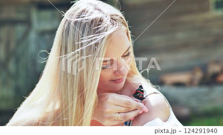 Young blond woman holding a colorful butterfly on her bare shoulder, enjoying a sunny summer day outdoors Young blond woman holding a colorful butterfly on her bare shoulder, enjoying a sunny summer day outdoors 124291940