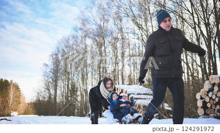Happy family enjoying a winter day outdoors, pulling a sled with children through snowy woods 124291972