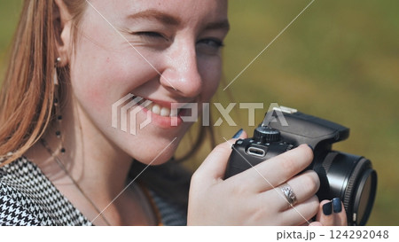 Professional camera balanced in hands, female photographer winking playfully during outdoor shoot, expressing creative joy 124292048