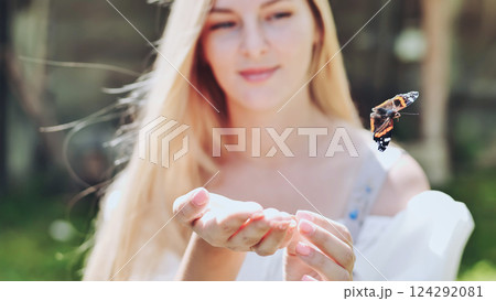 Delicate blonde holding iridescent butterfly, soft sunlight caressing her palms, connecting with fragile natural wonder 124292081