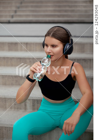 Women Enjoying Fitness Break While Sitting on Stairs and Drinking Water in Activewear Outdoors 124293048