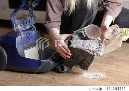 Woman holding household vacuum cleaner container clogged up with dust after an extensive cleaning 124293385