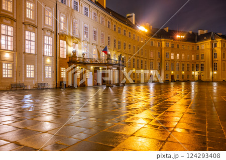 At dusk, the entrance door of Prague Castle features a balcony overlooking the Third Courtyard, with reflections on the wet stone pavement creating a serene atmosphere. 124293408
