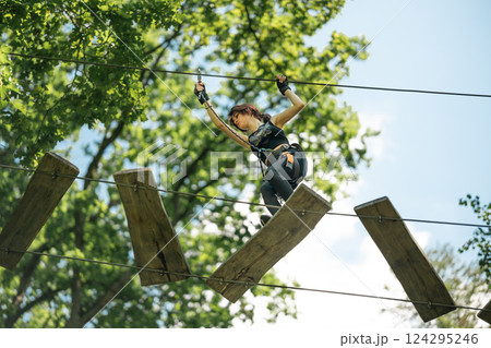 A determined woman successfully conquers the challenging high rope obstacle course set in the beauty of nature A determined woman successfully conquers the challenging high rope obstacle course set in the beauty of nature 124295246