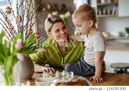 Mother and little son decorating pussy willows branches, putting easter eggs on them. 124295300