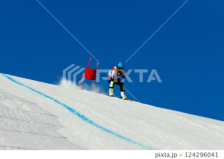 skier passes red gate down snow-covered slope during competitive downhill skiing 124296041