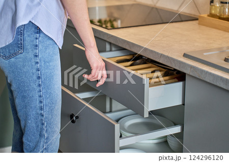 Person opening kitchen drawer with cutlery in cabinet 124296120