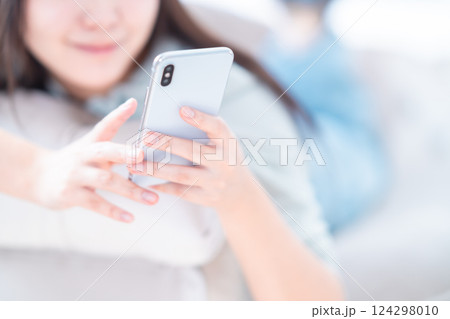 寝転んでリラックスしながらスマホを見る若い女性　顔無し 124298010